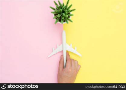 Flat lay design of travel in summer concept - Top view of a hand holding on an airplane and cactus on pink and yellow pastel color screen with copy space. travel summer trip on pastel color background