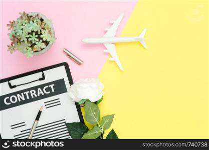 Flat lay design of working space - Top view layout of contract document, airplane and ink pen with white rose and tree on pink and yellow pastel color with copy space. Pastel working space background