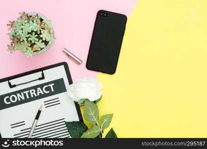 Flat lay design of working space  - Top view mock up of contract, pen and black screen smartphone with white rose and tree on pink yellow pastel color with copy space. Pastel working space background.
