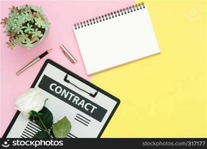Flat lay design of working space - Top view mockup of contract document, pen and white paper notebook with rose and tree on pink yellow pastel color with copy space. Pastel working space background.
