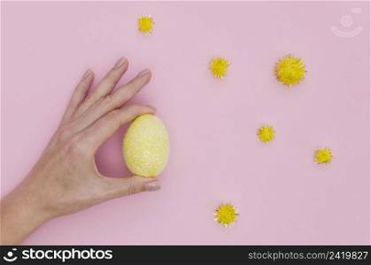 flat lay hand holding colorful easter egg with dandelions