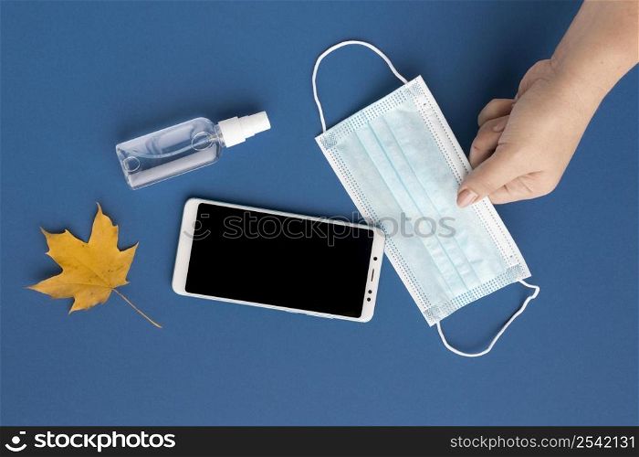 flat lay hand holding medical mask with smartphone autumn leaf