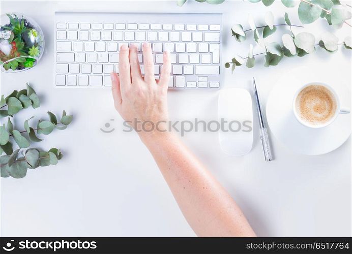 Flat lay home office workspace. Flat lay home office workspace, someones hand typing on white modern keyboard and silver green twigs