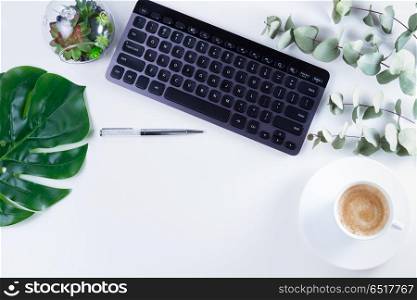 Flat lay home office workspace. Flat lay home office workspace with black keyboard and green leaves on white background