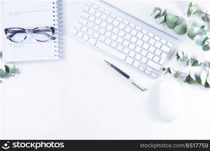 Flat lay home office workspace. Flat lay home office workspace with white modern keyboard, notebook and green eucaliptus twigs