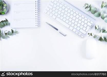 Flat lay home office workspace. Flat lay home office workspace with white modern keyboard, notebook and silver green twigs