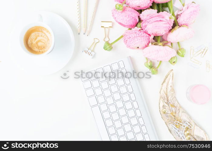 Flat lay home office workspace - modern keyboard with cup of coffee and pink ranunculus flowers. Top view home office workspace