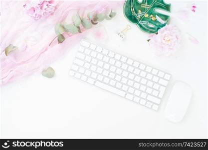 Flat lay home office workspace - modern keyboard with female accessories and peony flowers, copy space on white background. Top view home office workspace
