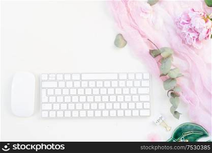 Flat lay home office workspace - modern keyboard with female accessories and peony flowers with copy space. Top view home office workspace