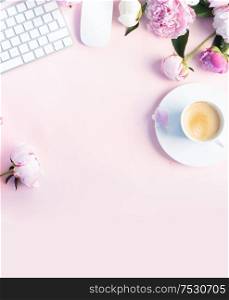 Flat lay home office workspace - modern keyboard with female accessories and fresh peony flowers, copy space on pink desk background. Top view home office workspace