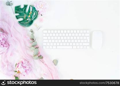 Flat lay home office workspace - modern keyboard with female accessories and peony flowers. Top view home office workspace