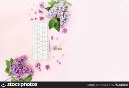 Flat lay home office workspace - modern keyboard with lilac flowers and copy space. Top view home office workspace