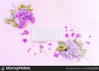 Flat lay home office workspace - modern keyboard with lilac flowers and copy space, toned. Top view home office workspace