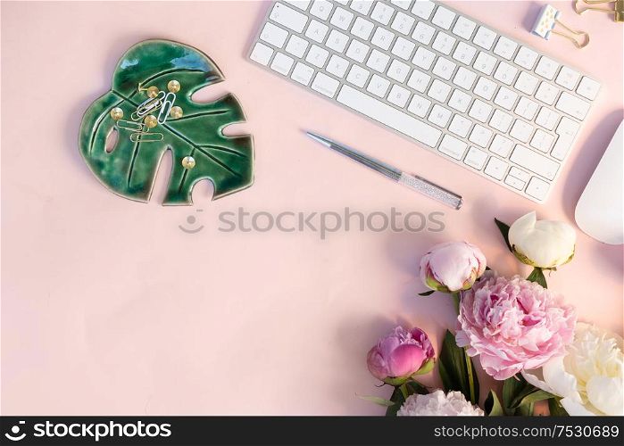 Flat lay home office workspace - modern white keyboard with and peony flowers, copy space on pink background. Top view home office workspace