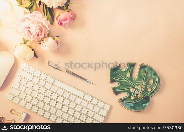 Flat lay home office workspace - modern white keyboard with and peony flowers, copy space on pink background, toned. Top view home office workspace