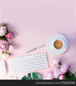 Flat lay home office workspace - modern white keyboard with cup of coffee and peony flowers, copy space on pink desk background. Top view home office workspace