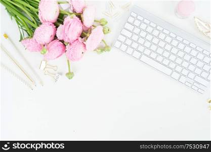 Flat lay home office workspace - modern white keyboard with female accessories and ranunculus flowers. Top view home office workspace