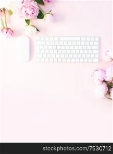 Flat lay home office workspace - modern white keyboard with peony flowers, copy space on pink desk background. Top view home office workspace