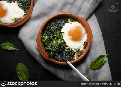 Flat lay image with backed spinach and eggs in clay plates on a gray kitchen towel