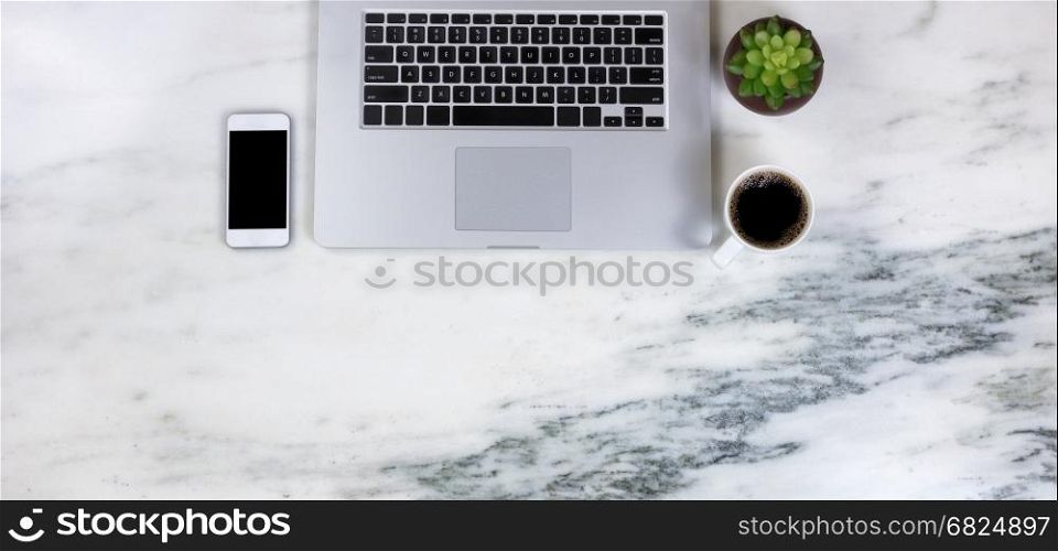 Flat lay of a partial laptop, plant, smartphone and dark coffee on natural marble desktop