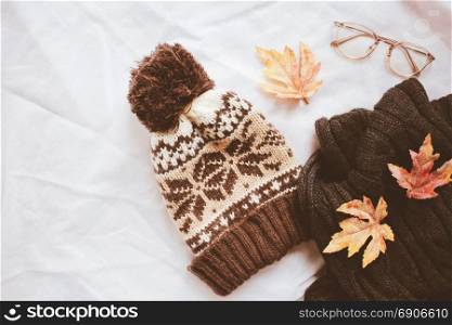 Flat lay of autumn fashion style, scarf, knitted hat and eyeglasses with maple leaves on white sheet background