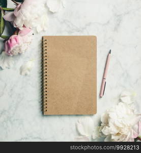 Flat-lay of Beautiful peony flowers  and closed notebook on white marble background, top view