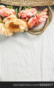 Flat-lay of Beautiful peony flowers in straw bag over grey linen table cloth background, top view, copy space