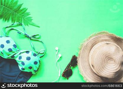 Flat lay of bikini and accessories with fern leaves on green background, Summer and Tropical concept with copy space