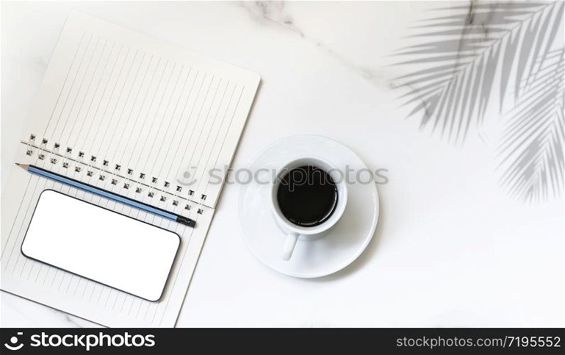 Flat lay of black coffee in white ceramic cup, smartphone mock up, pencil with spiral notepad and palm leaf shadow on white marble tabletop, hobby and relaxing time concept