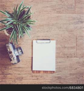 Flat lay of blank clipboard and vintage film camera with green plant on wooden background, retro filter styled