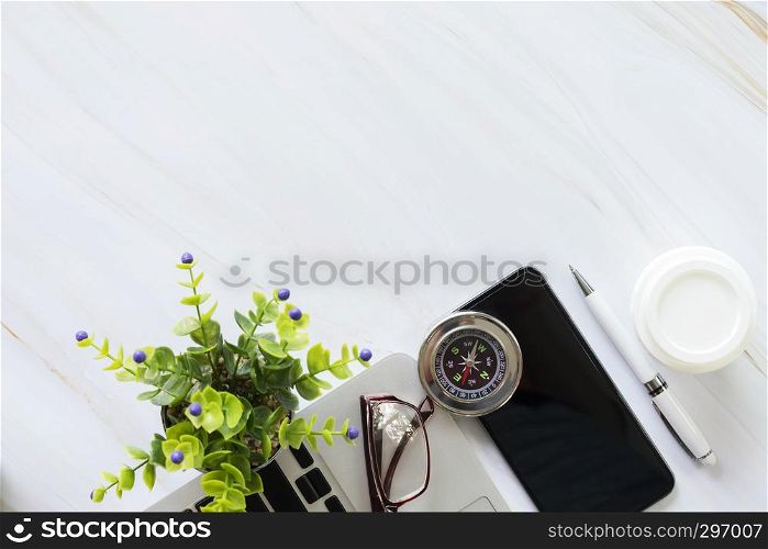 Flat lay of business accessories on desk, mobile, laptop, pen, coffee cup, glasses, compass and plant pot.