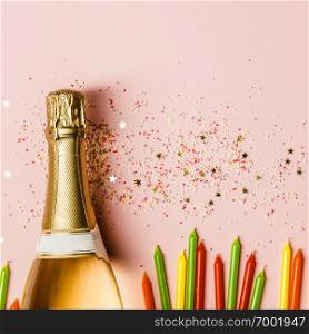 Flat lay of Celebration. Champagne bottle with ice cream sprinkles, golden star sprinkles and birthday candles on pink background. Top view. Flat lay of Celebration. Champagne bottle with sprinkles on pink background.