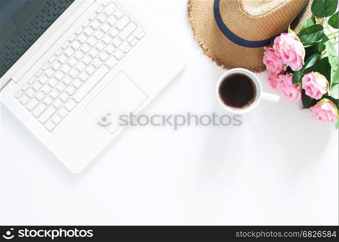 Flat lay of computer laptop with casual hat, a cup of coffee and pink roses, Top view on white background with copy space