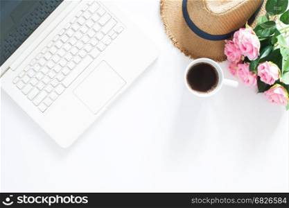 Flat lay of computer laptop with casual hat, a cup of coffee and pink roses, Top view on white background with copy space