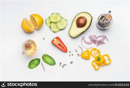 Flat lay of fresh salad vegetables ingredients: avocado, cucumber, paprika, onion, lemon , olives oil and vinegar on white desk background, top view. Healthy lifestyle and vegetarian eating concept