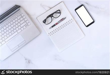 Flat lay of laptop, smartphone and eyeglasses with various stationeries on white marble tabletop