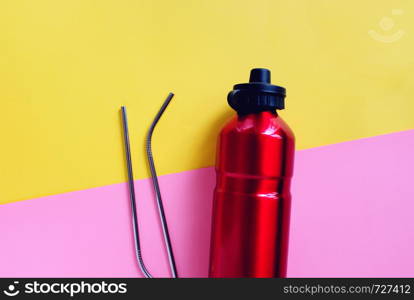 Flat lay of metallic stainless straws and reusable bottle for drink on bright pink and yellow background, sustainable product lifestyle and zero waste concept, copy space