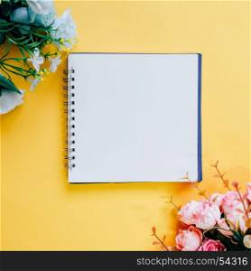 Flat lay of minimal workspace blank notebook with flower on yellow background, spring and summer concept