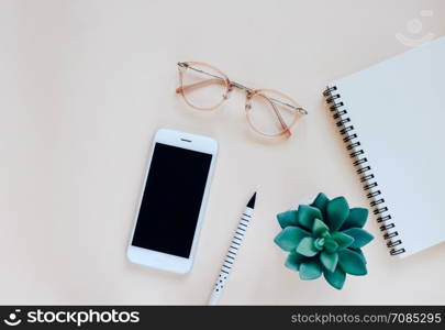 Flat lay of minimal workspace desk with smartpohne, notebook, pen, eyeglasses and plant