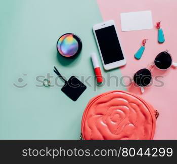 Flat lay of pink cute woman bag open out with cosmetics, accessories, tag card and smartphone on colorful background with copy space&#xD;