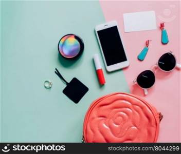 Flat lay of pink cute woman bag open out with cosmetics, accessories, tag card and smartphone on colorful background with copy space&#xD;
