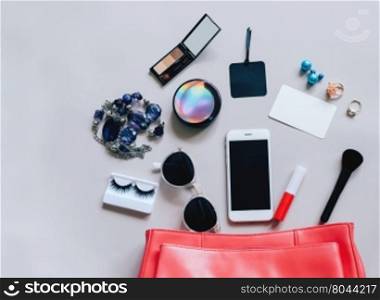 Flat lay of pink leather woman bag open out with cosmetics, accessories, tag card and smartphone on grey background with copy space&#xD;