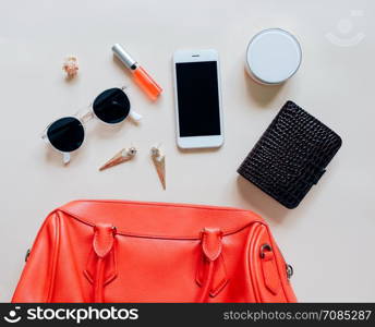 Flat lay of red leather woman bag open out with cosmetics, accessories and smartphone on yellow background