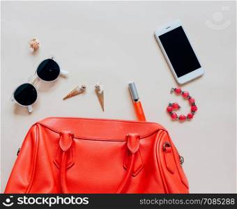 Flat lay of red leather woman bag open out with cosmetics, accessories and smartphone on yellow background