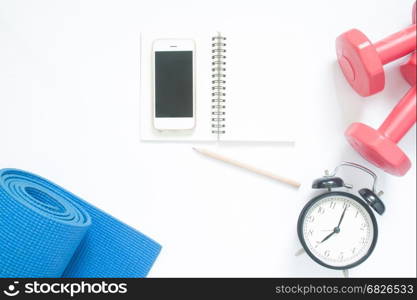 Flat lay of smartphone with sport yoga equipments, notebook and clock on white background