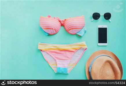 Flat lay of summer items with colorful bikini, sunglasses , hat and smartphone on green background, copy space