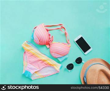 Flat lay of summer items with colorful bikini, sunglasses , hat and smartphone on green background, copy space
