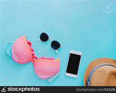 Flat lay of summer items with colorful bikini, sunglasses, hat and smartphone on green background, copy space