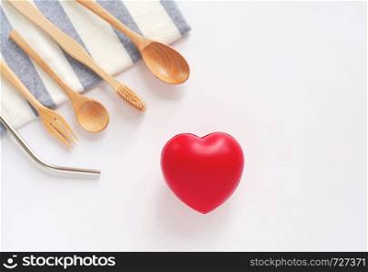 Flat lay of sustainable products, wooden spoon, stainless straw on table cloth with red heart on white background, eco friendly and zero waste concept