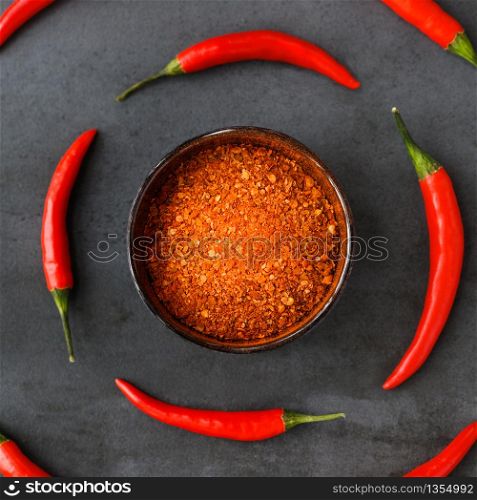 Flat lay of Thai red fresh hot chilli peppers with green tails and dried red chilli flakes in bowl on black stone background. Food pattern. Popular spices.